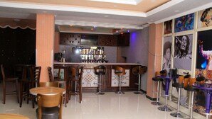 Uma área de bar com banquetas, um balcão com garrafas e piso ladrilhado.