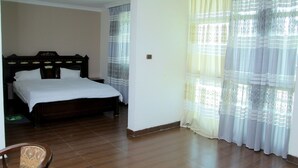 Quarto com cama, cortinas e piso de madeira.