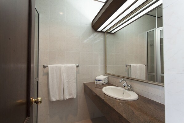 A modern bathroom with a glass shower door, a white sink, and a large mirror. - Queens Hotel (Kandy)