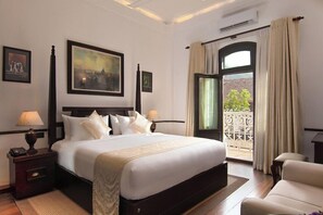 Ein Hotelzimmer mit einem großen Bett, einem Nachttisch, einer Lampe, einem Bild an der Wand und Blick ins Freie.
