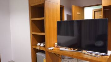 A room with a wooden desk, a flat-screen TV, a remote control, and a small refrigerator.