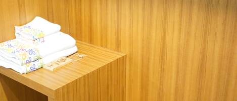 Un armario de madera con espejo y una mesita con ropa doblada y zapatillas.