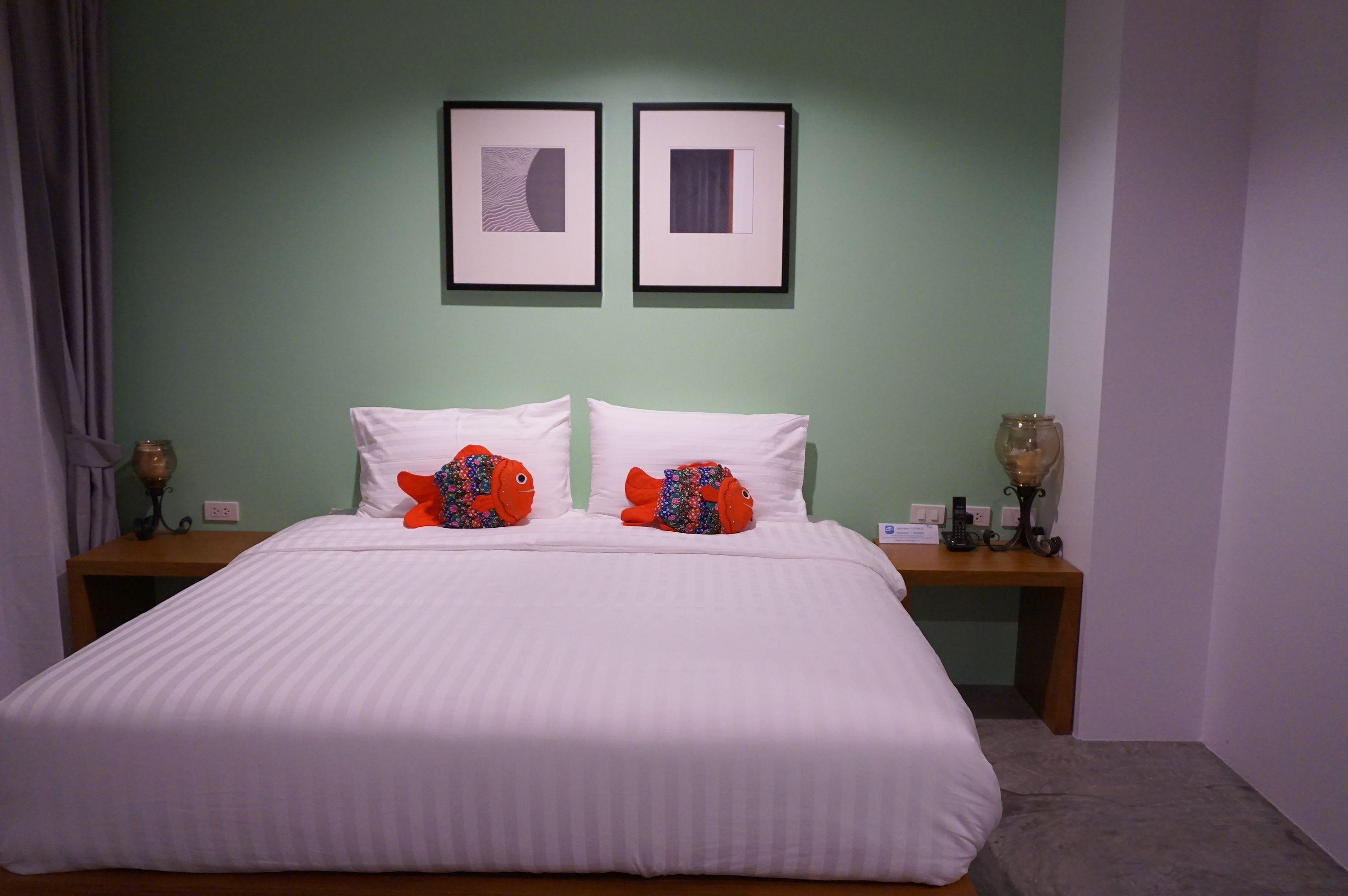 Un lit avec une literie blanche et deux oreillers, une table de chevet avec une lampe, et deux tableaux encadrés accrochés au mur.