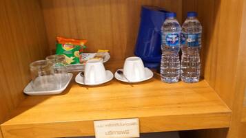 A small wooden cabinet with a label reading "Café & Food Service" containing a coffee machine, cups, a bag of snacks, and two water bottles.