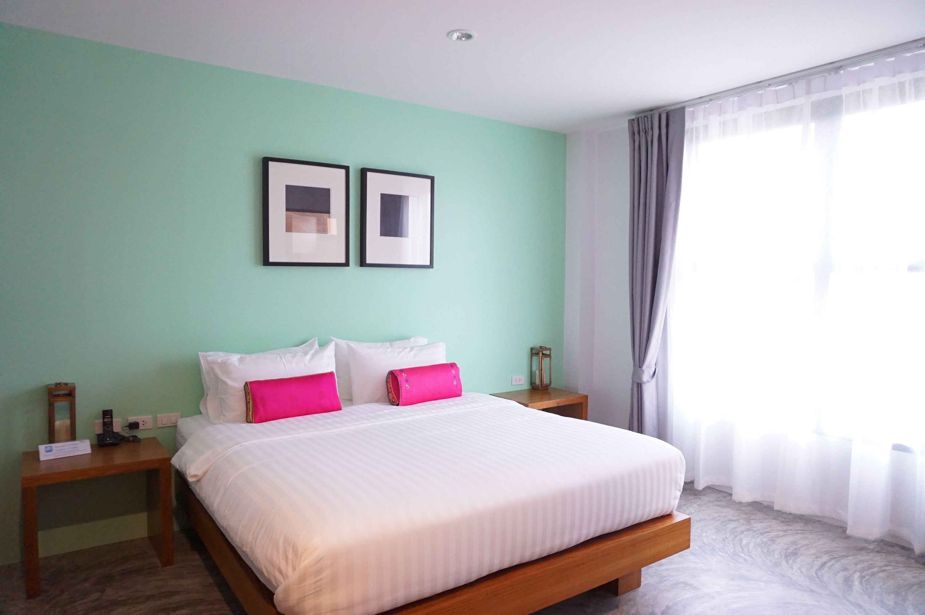 A hotel room with a large bed, two bedside tables, a nightstand, a framed picture on the wall, and a window with curtains.