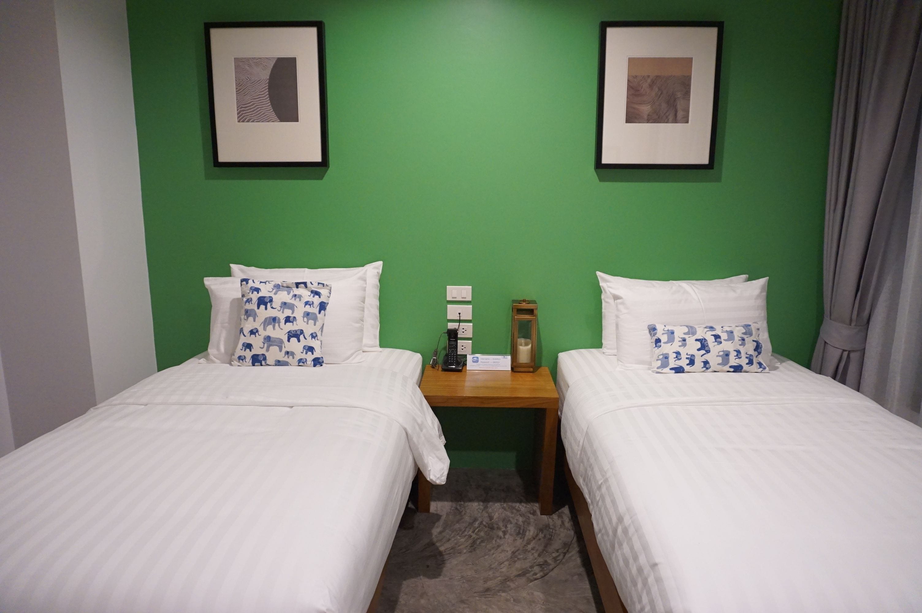Habitación de hotel con dos camas, paredes verdes, obras de arte enmarcadas y una mesita de noche con lámpara y teléfono.
