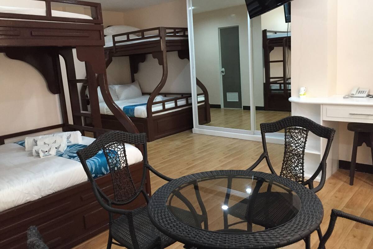 A room with bunk beds, a glass table, wicker chairs, a desk, and a mirror.