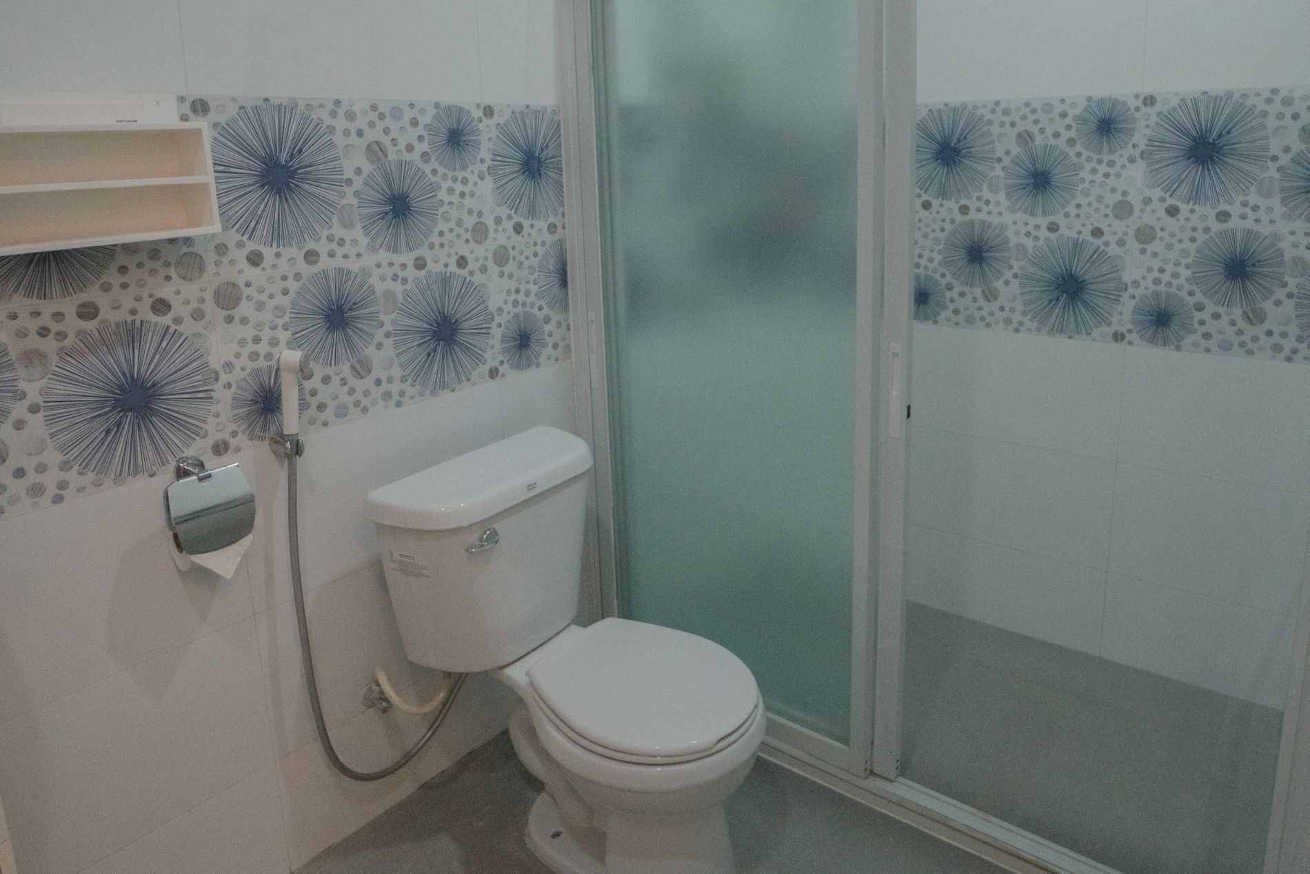 Un baño con inodoro, ducha y pared con diseño.
