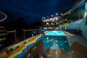 A swimming pool with a dolphin slide, lounge chairs, and a building with balconies in the background. - Skylodge Resort (Coron)