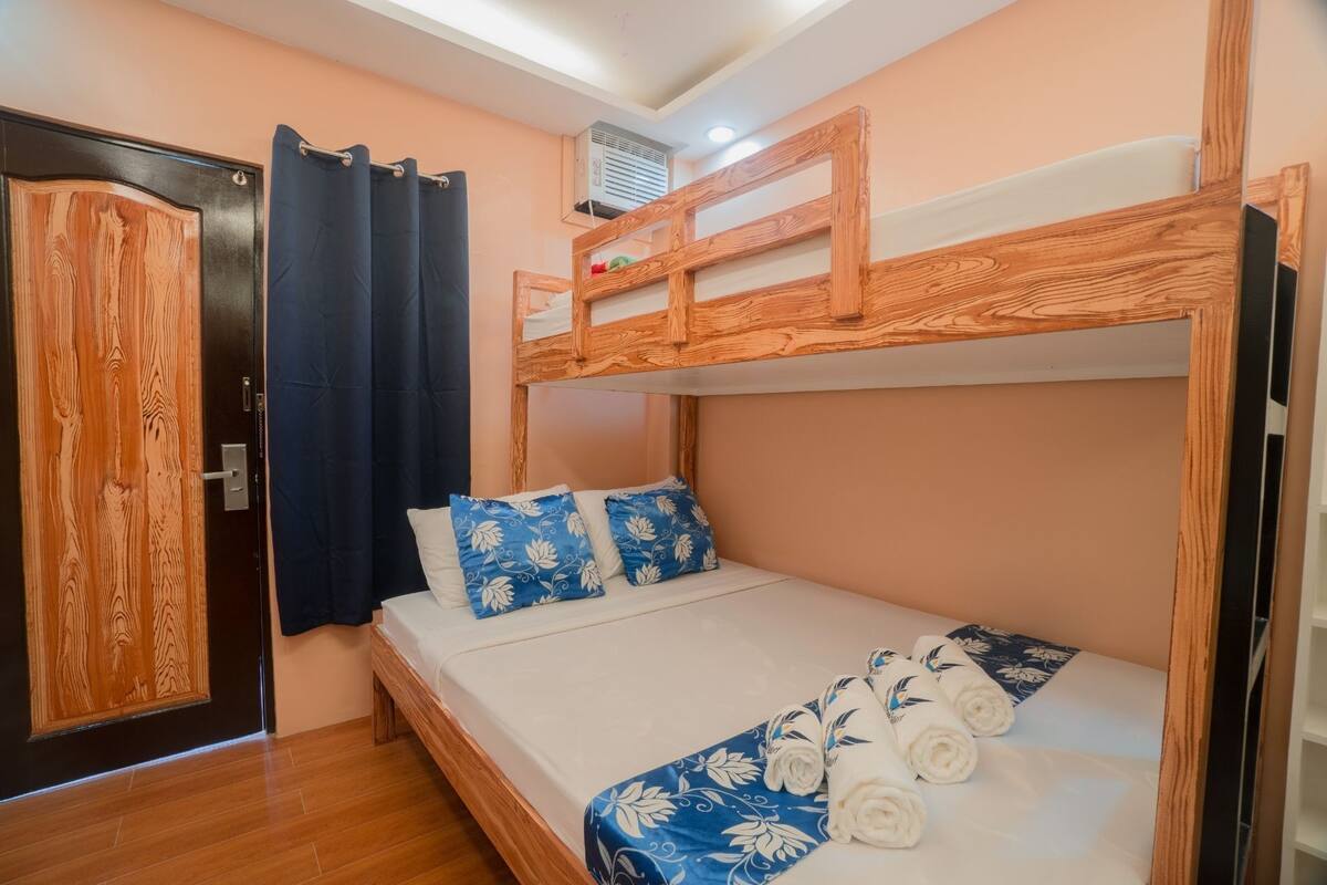 A bunk bed room with a wooden headboard, a door with a patterned design, and a window with curtains.