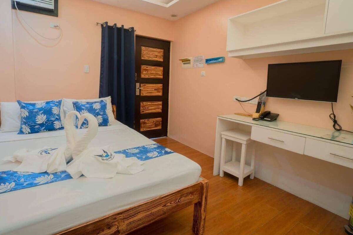 A hotel room with a bed, a desk, a TV, and a wooden door.