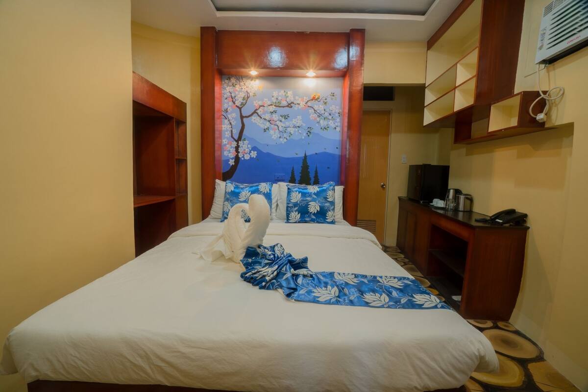 A hotel room with a bed, a desk, and a wall-mounted air conditioner.