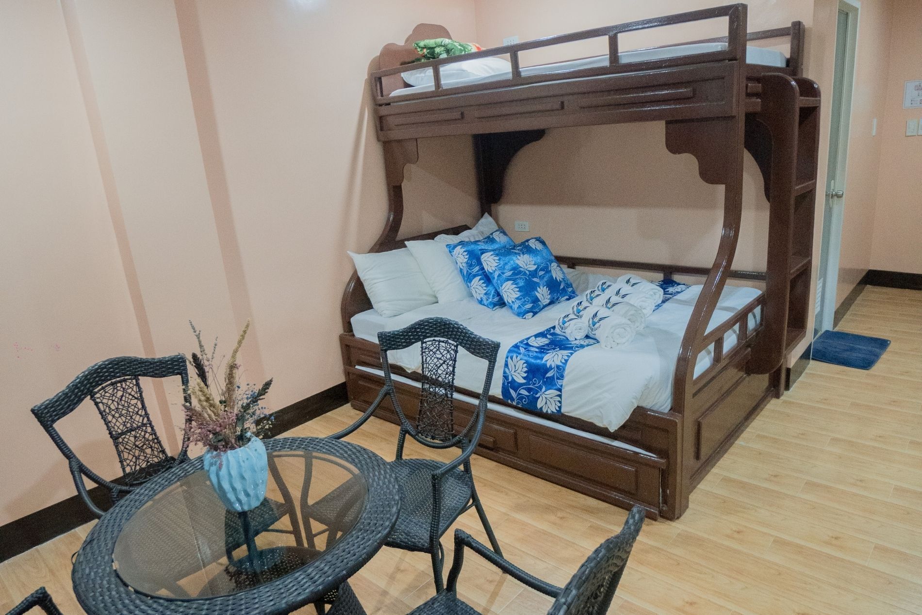 A bunk bed with a wooden frame and white bedding, a round glass table with chairs, and a small potted plant.