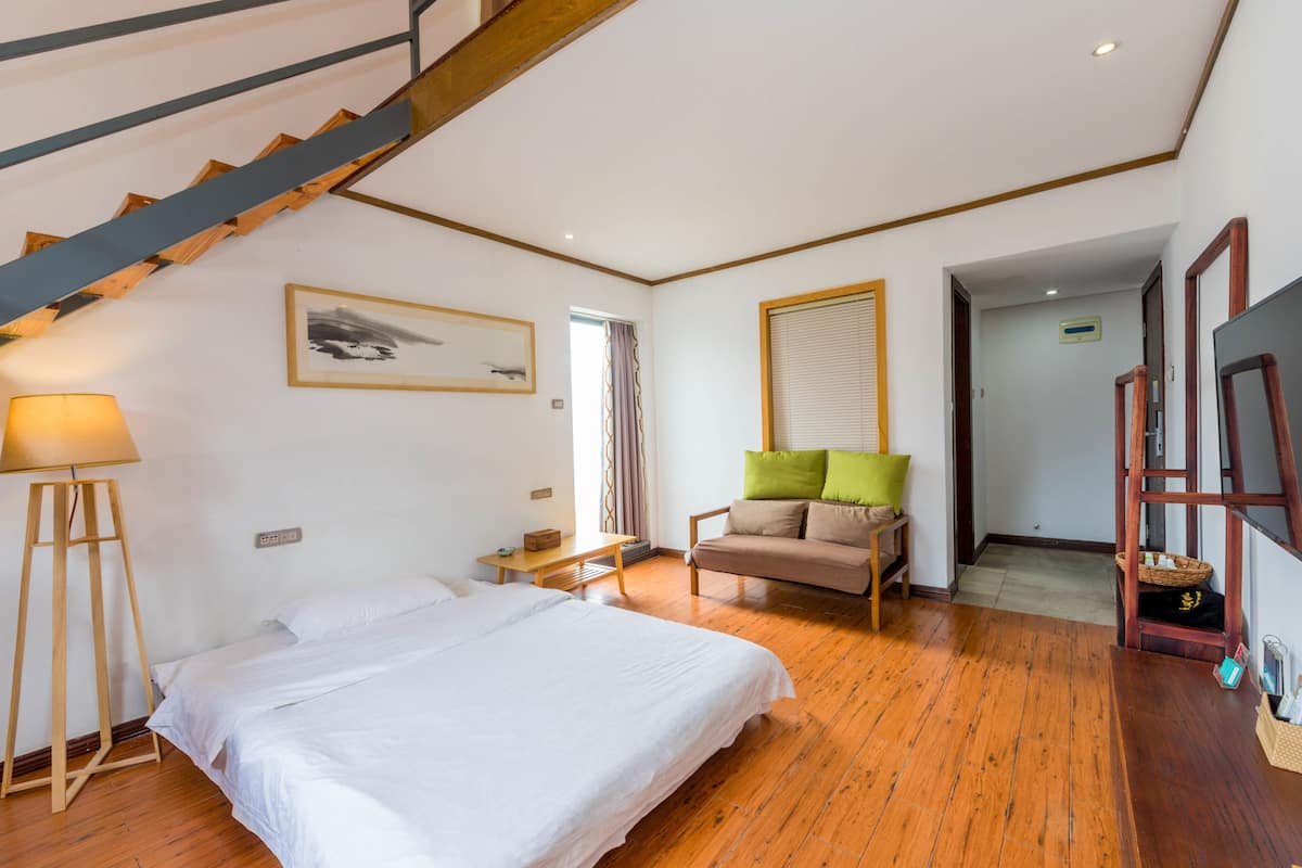 A bedroom with a bed, a chair, a lamp, a painting, and a staircase.