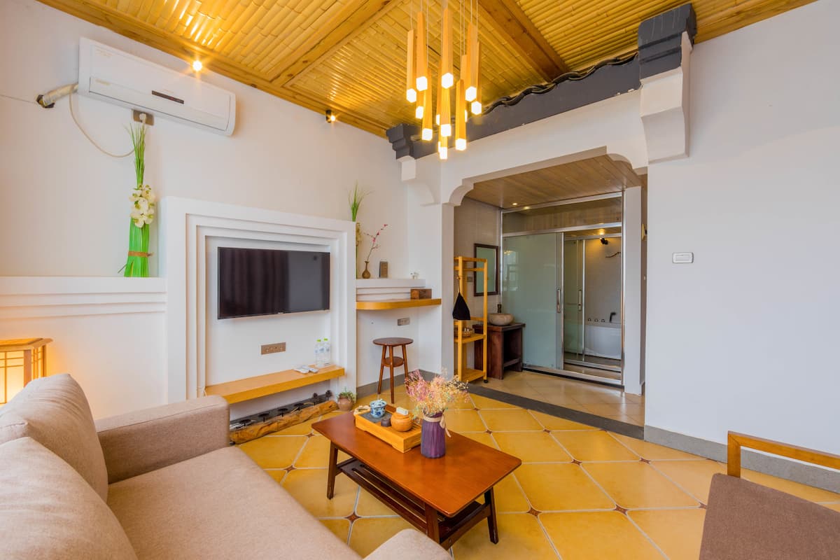 A modern living room with a sofa, coffee table, and TV. There is a wooden ceiling and a tiled floor.