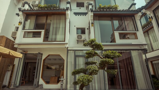 Un edificio de varios pisos con balcones, ventanas amplias y un bonsái en el patio.