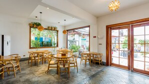 Un espacio interior amplio con mesas y sillas de madera, un ventanal con vistas al exterior y una lámpara colgante.
