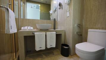 A modern bathroom with a glass shower enclosure, a large sink with a bowl, two towels hanging on the sink, a hairdryer, and a toilet.
