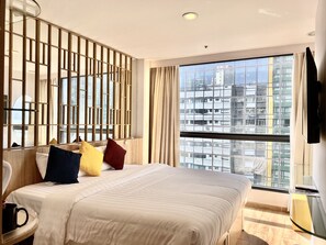 A hotel room with a large bed, a bedside table with a black mug, a TV mounted on the wall, and a large window offering a city view. - IW Hotel (Kowloon)