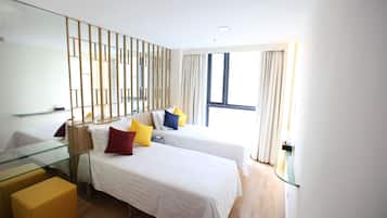 Quarto de hotel moderno com duas camas de solteiro, uma mesa de vidro e uma janela grande com cortinas.