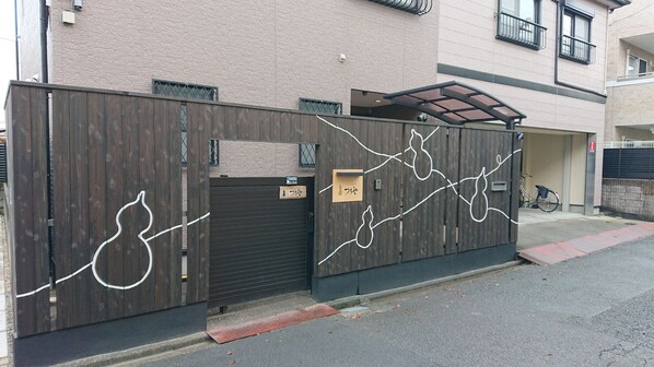 A gated entrance with a wooden fence, a closed garage door, and a bicycle parked inside. - Showwa no yado Tsuchiya (Nagoya)