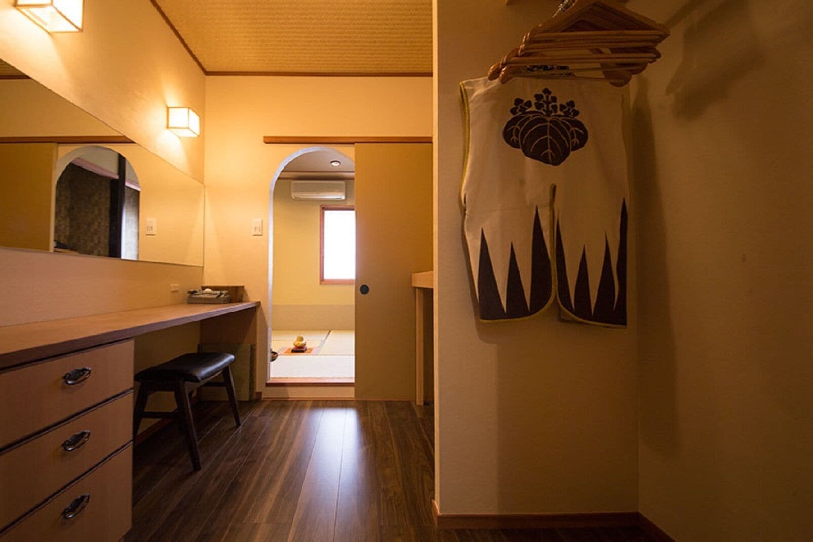 Une chambre d’hôtel avec un bureau en bois, une chaise, un miroir et un porte-serviettes avec des serviettes.