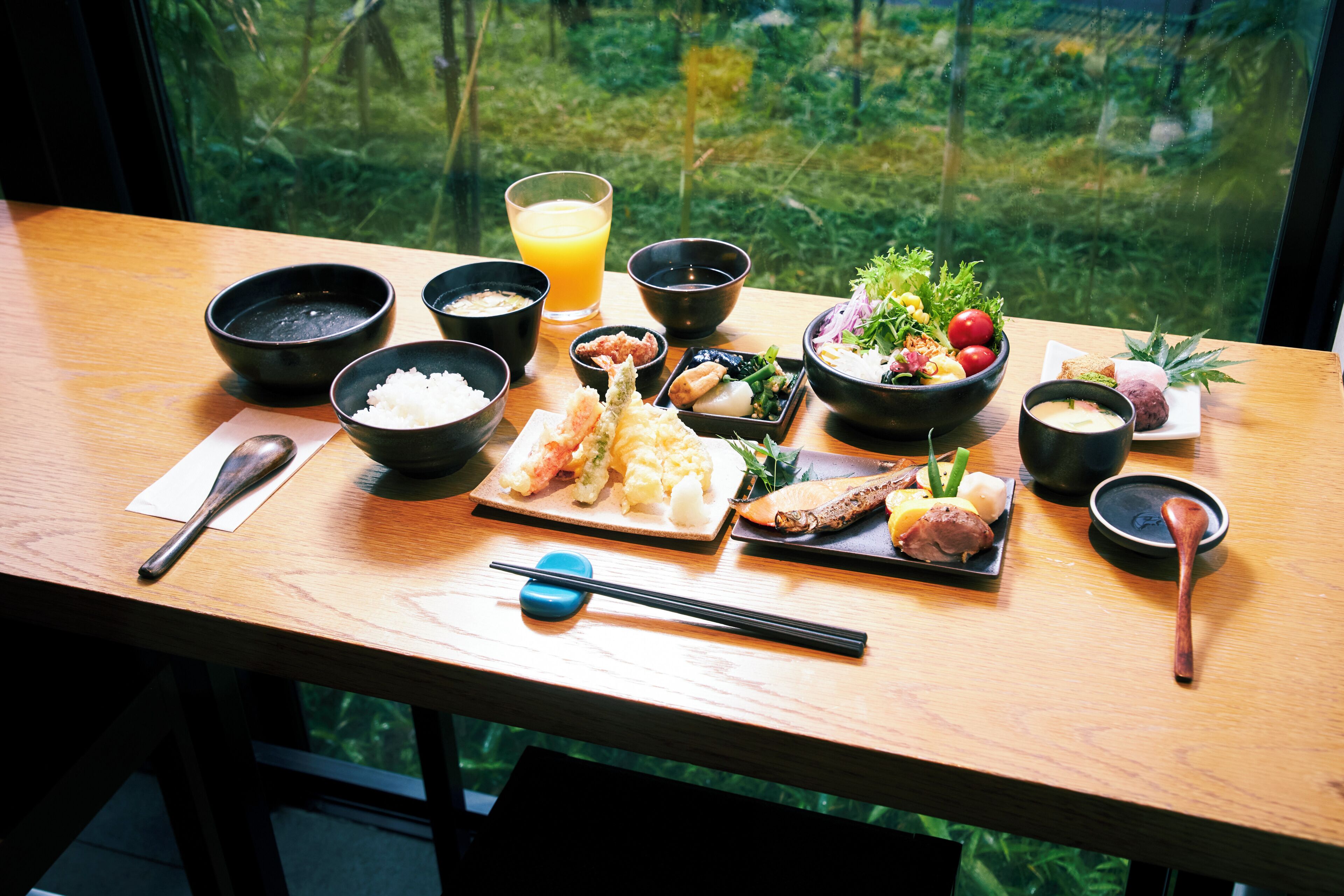 A wooden table with various dishes, including rice, vegetables, and fish, and a glass of orange juice.