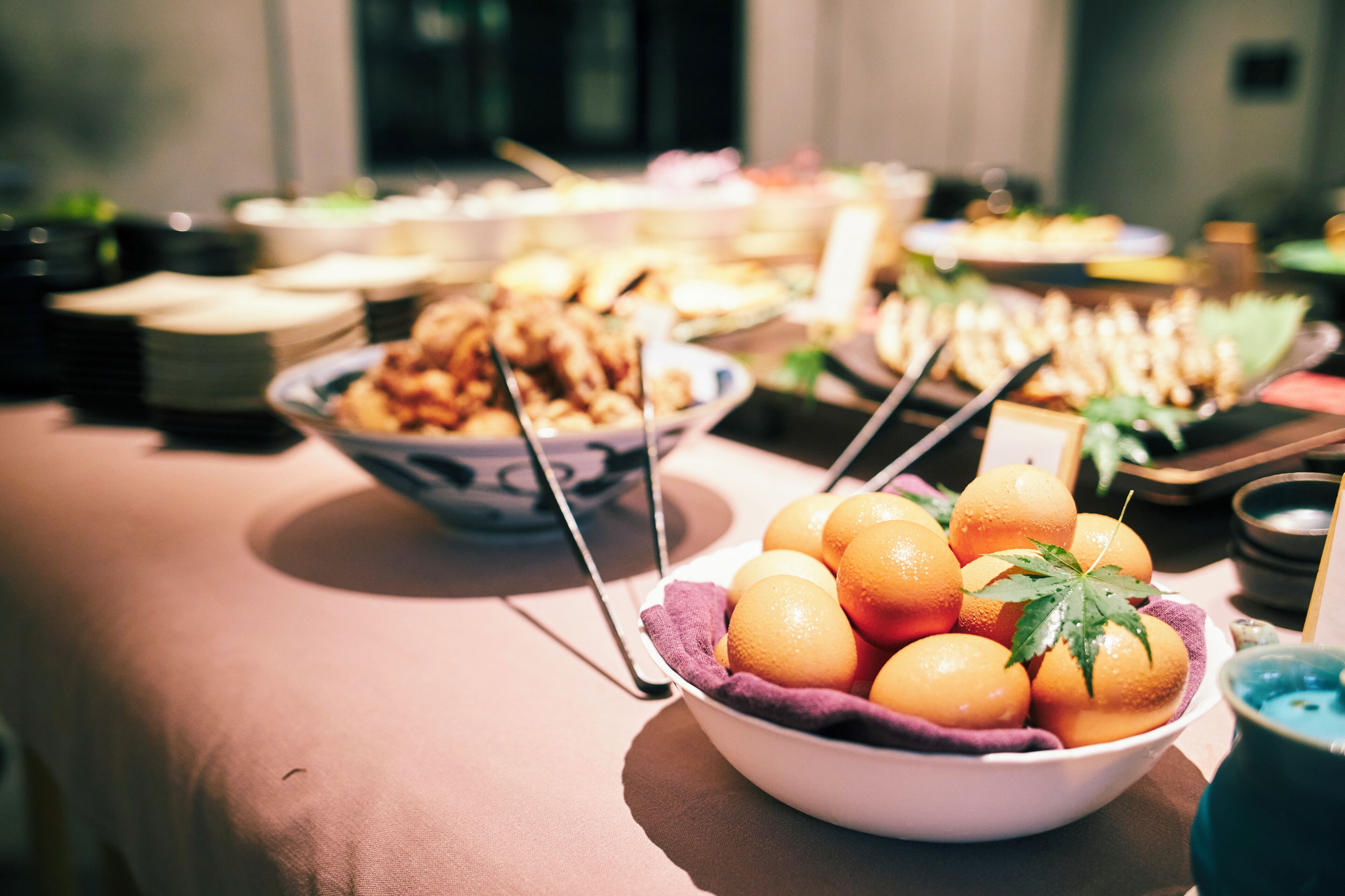A buffet table with various dishes and a bowl of oranges.