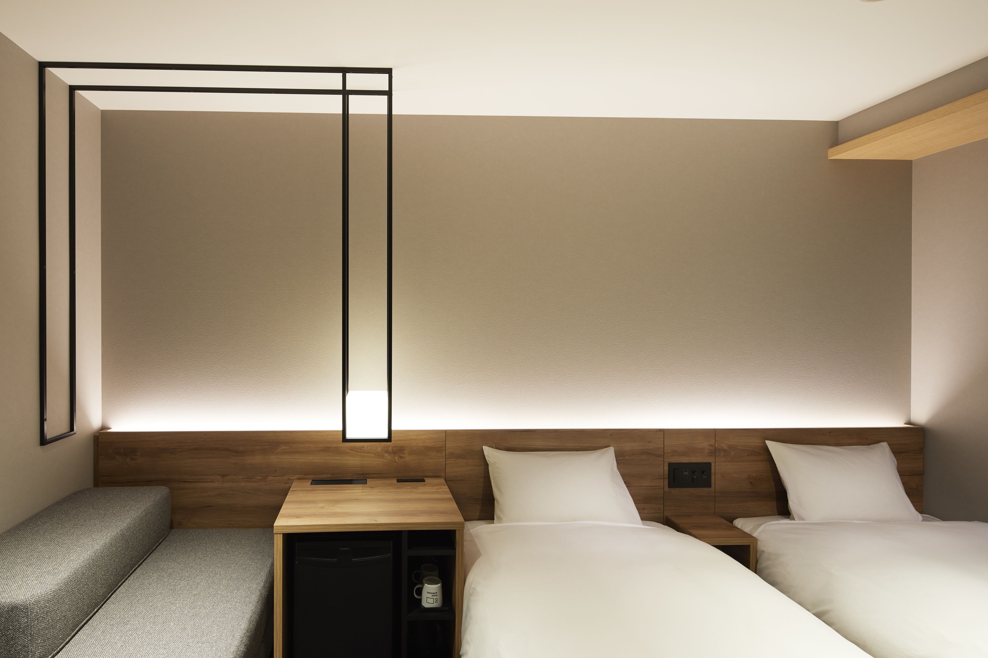 A modern hotel room with two beds, a small seating area, and a wooden headboard.