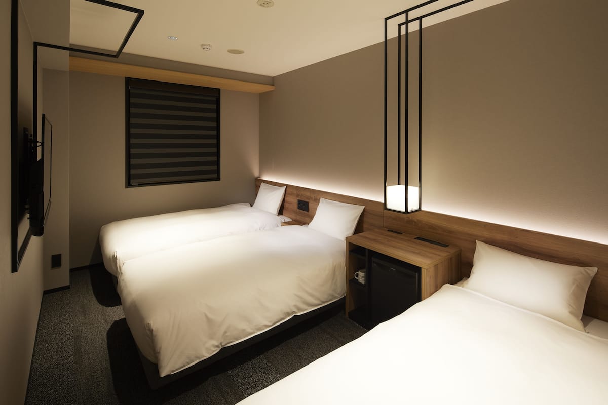 A hotel room with two beds, a wooden headboard, a nightstand, and a wall-mounted TV.