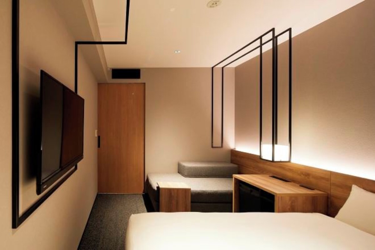A modern hotel room with a large bed, a desk, a television, and a wardrobe.