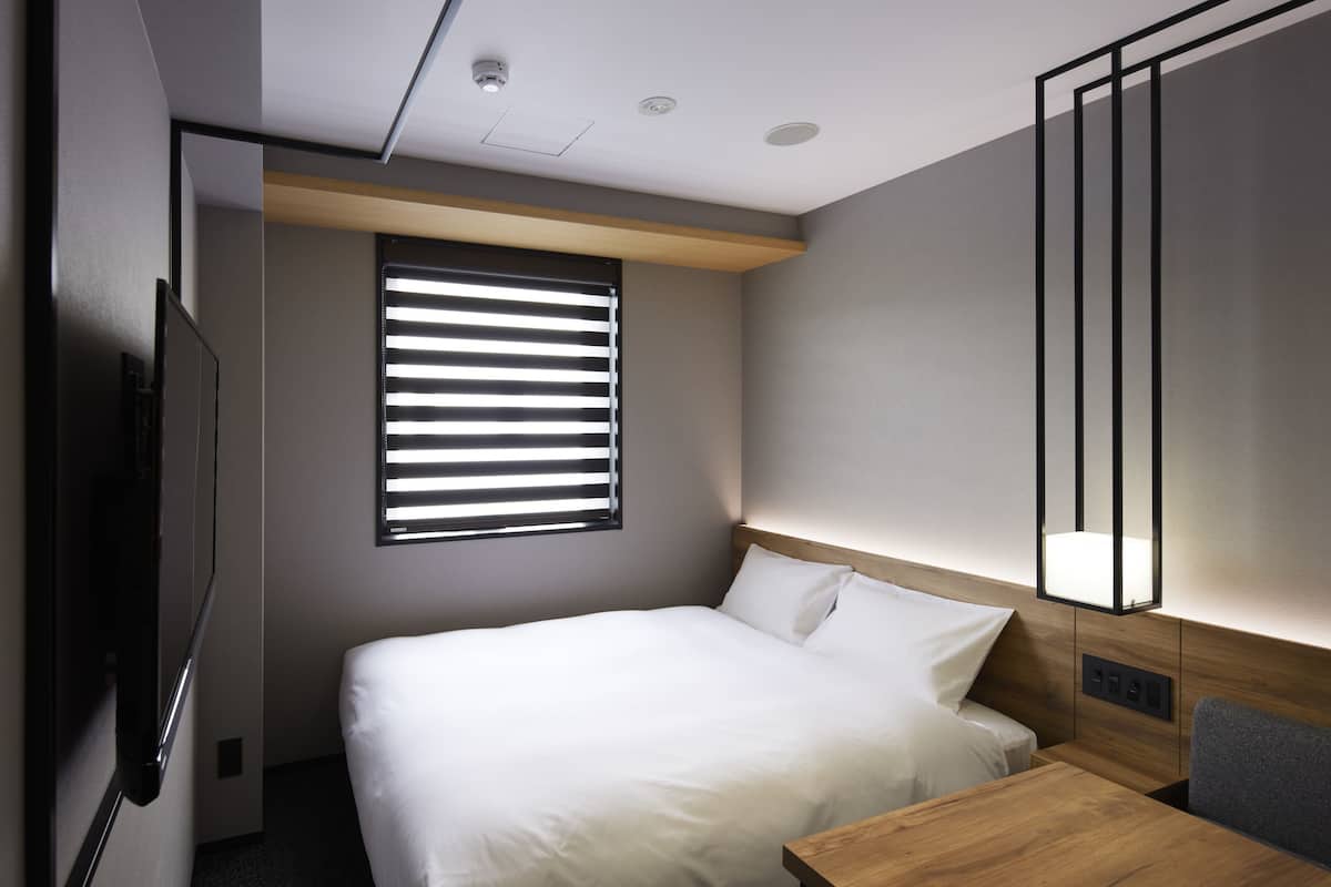 A modern hotel room with a bed, bedside table, and a large mirror.