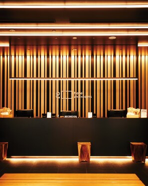 A hotel reception area with a modern design, featuring a reception desk, a waiting area with seating, and a vertical wooden panel wall. - hotel androoms Shin-Osaka (Osaka)