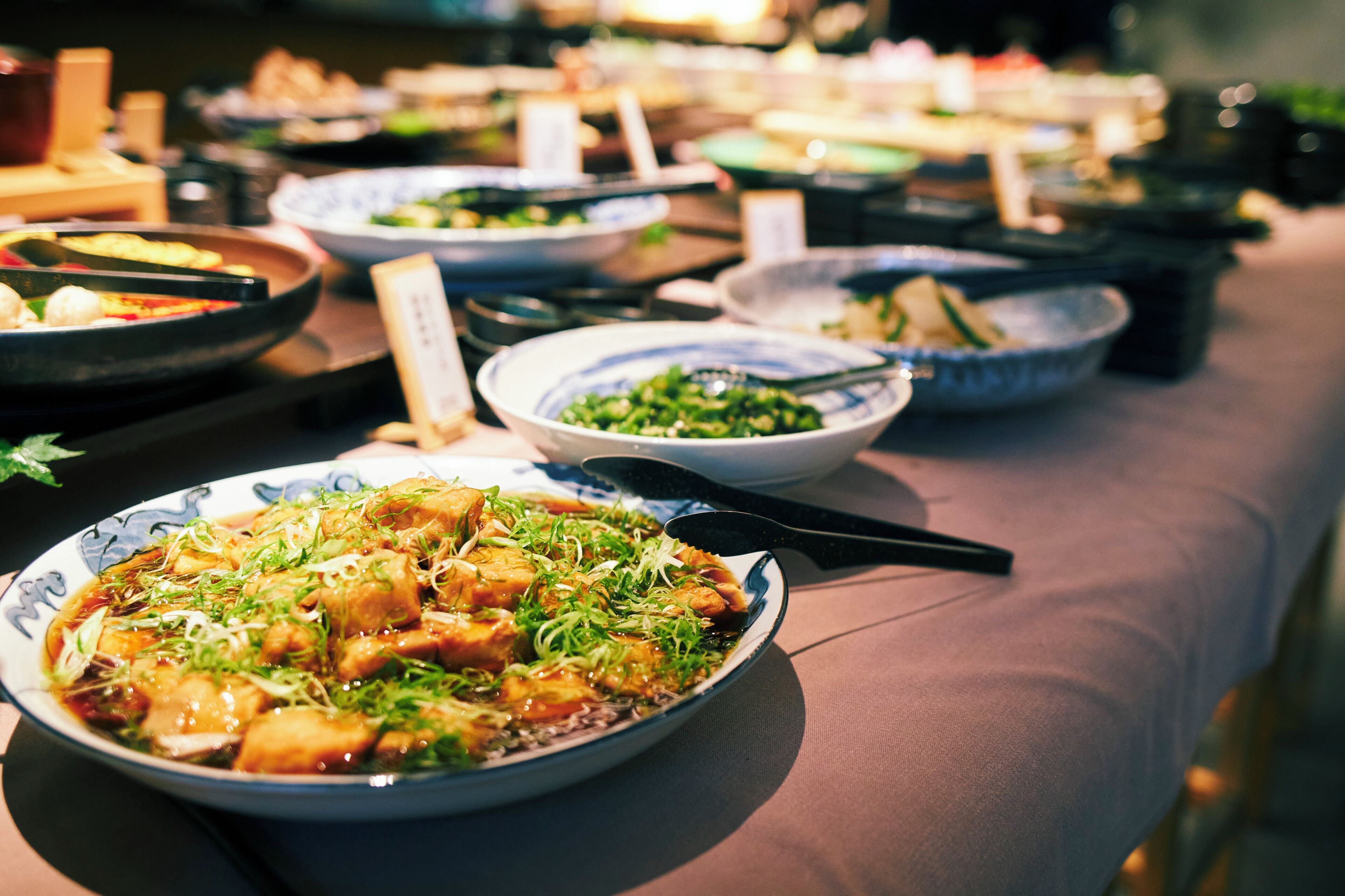 A table set with various dishes, including a bowl of food with greens and a plate with a different dish.