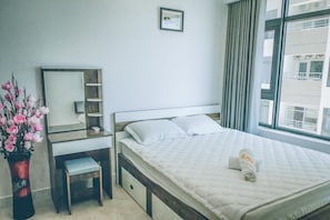 A hotel room with a bed, a bedside table, a mirror, a small stool, and a window with curtains.
