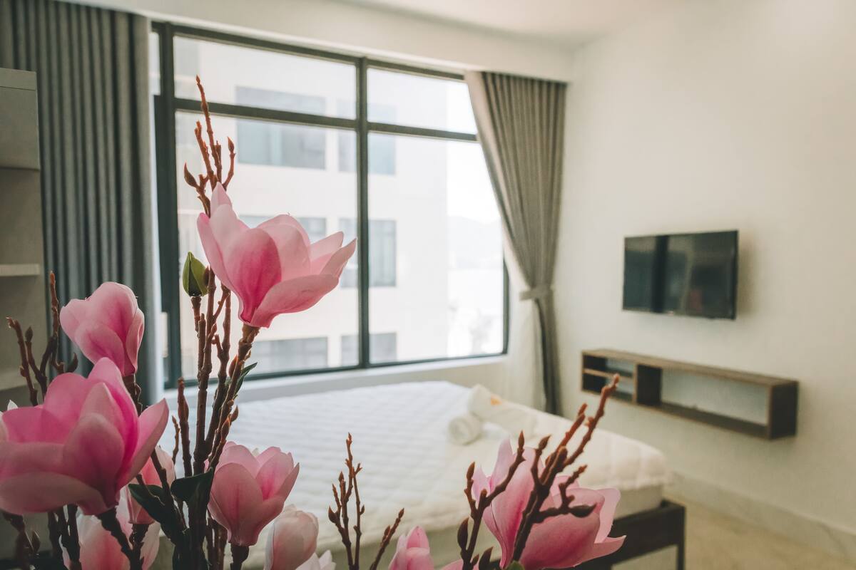 Une chambre d’hôtel dotée d’une grande fenêtre, d’un lit, d’une table de chevet et d’un téléviseur à écran plat fixé au mur.