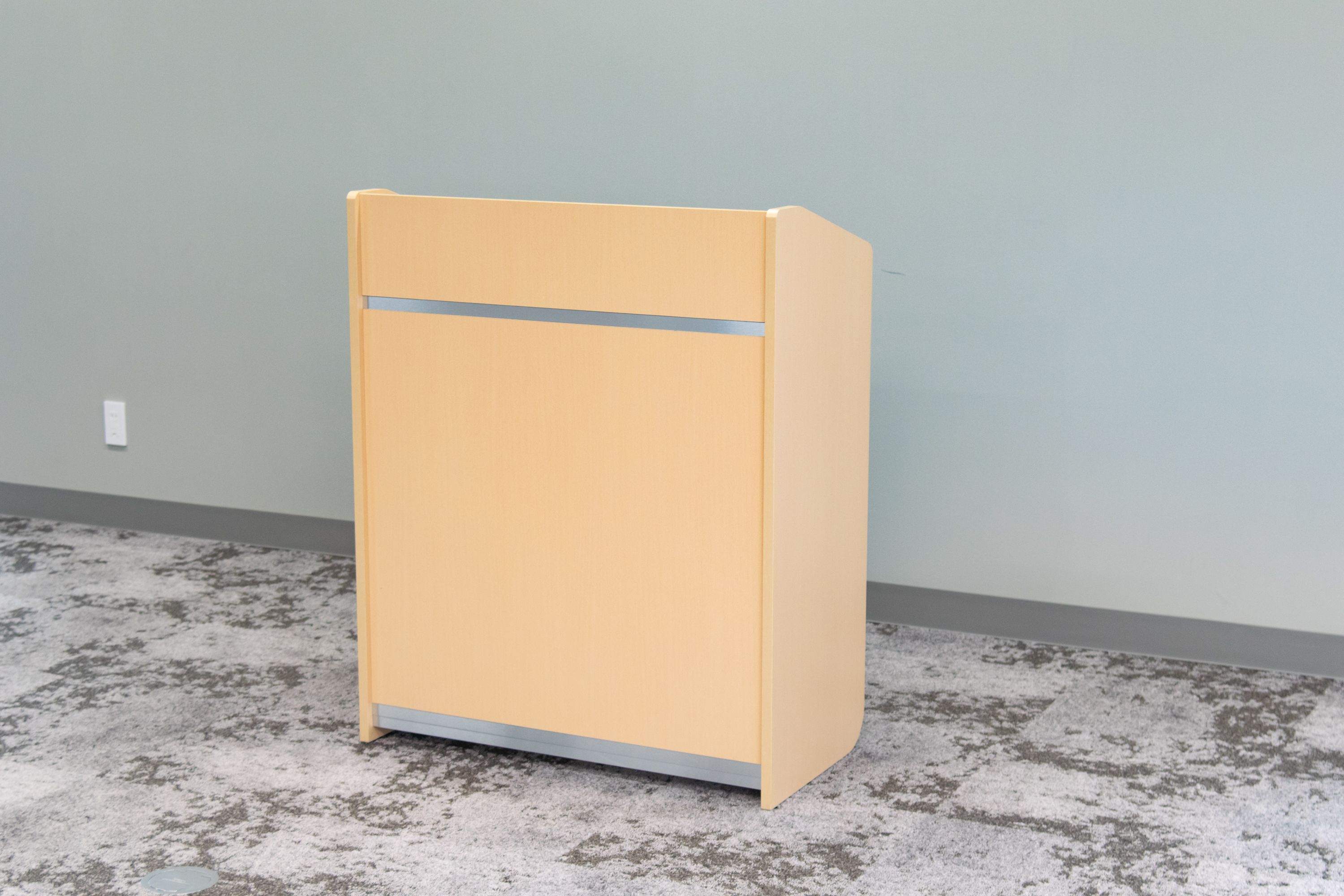 Een geel archiefkastje voor een lichtgrijze muur met een gestructureerde vloer.
