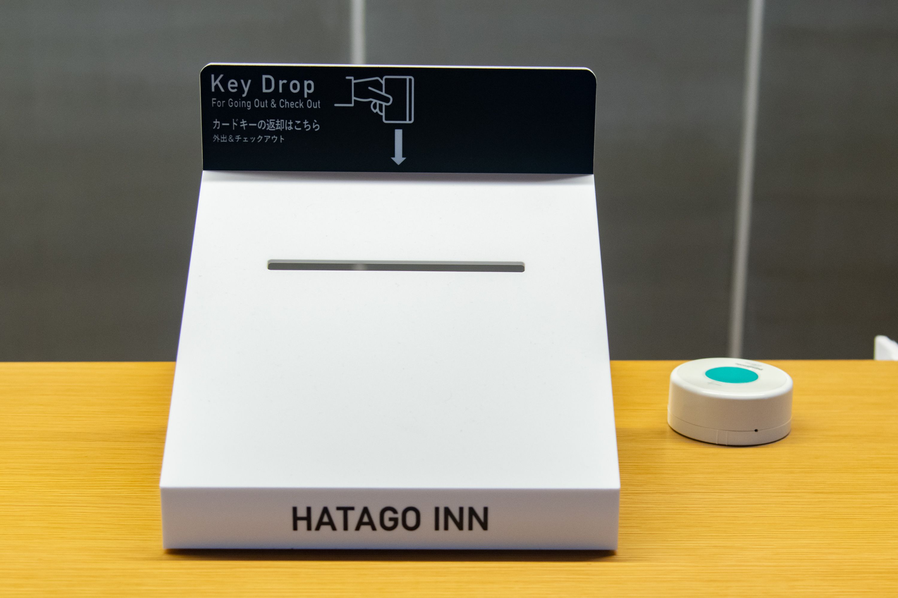 A key drop station with a sign indicating 'Key Drop For Going Out & Check Out' and a small device on the table.