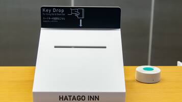 A key drop station with a sign indicating 'Key Drop For Going Out & Check Out' and a small device on the table.