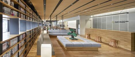 A modern hotel lobby with wooden floors, a long reception desk, and a seating area with a sofa and a small table.