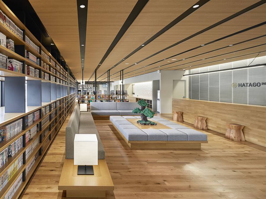 Een moderne hotellobby met houten vloeren, een lange receptiebalie en een zithoek met een bank en een klein tafeltje.