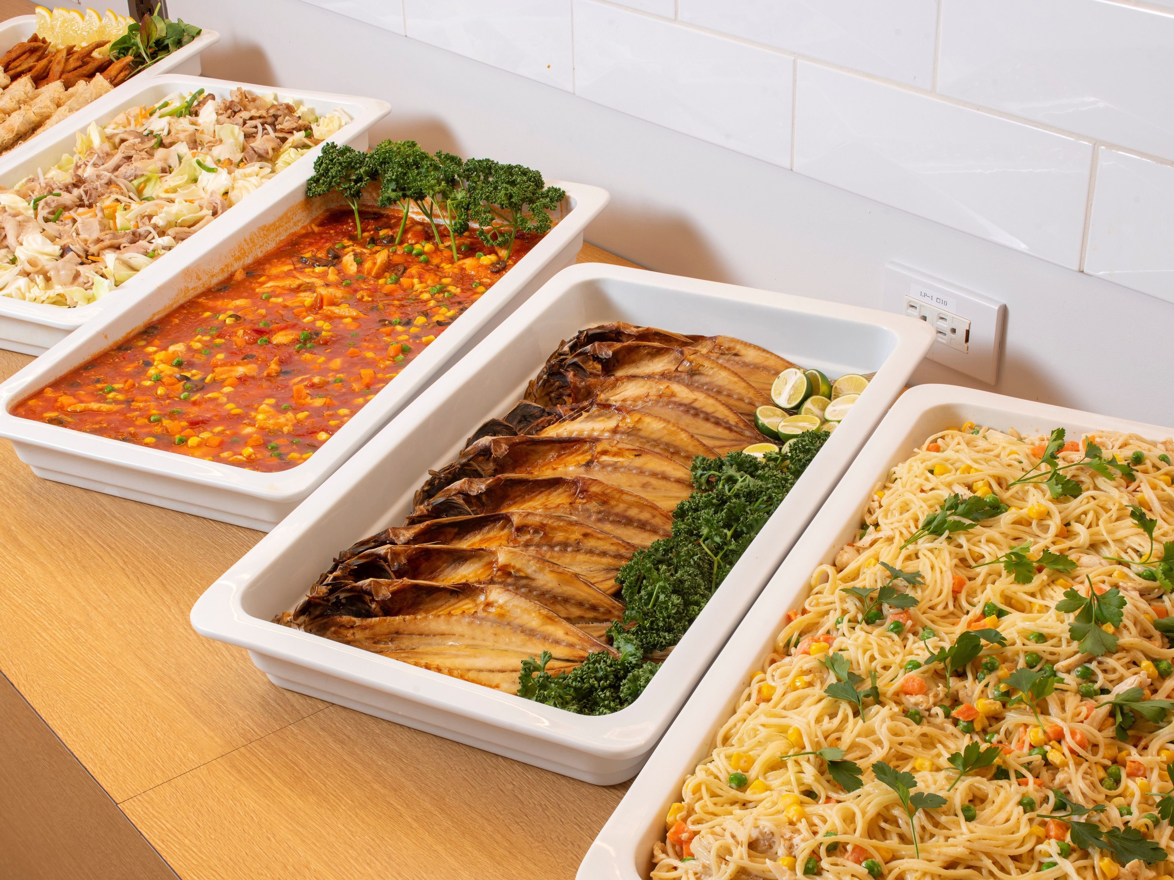 Een buffet met diverse gerechten, waaronder pasta, een visfilet en een groentegratin.
