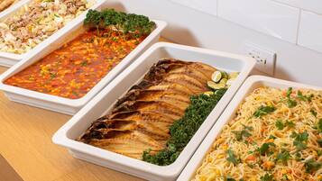 Een buffet met diverse gerechten, waaronder pasta, een visfilet en een groentegratin.