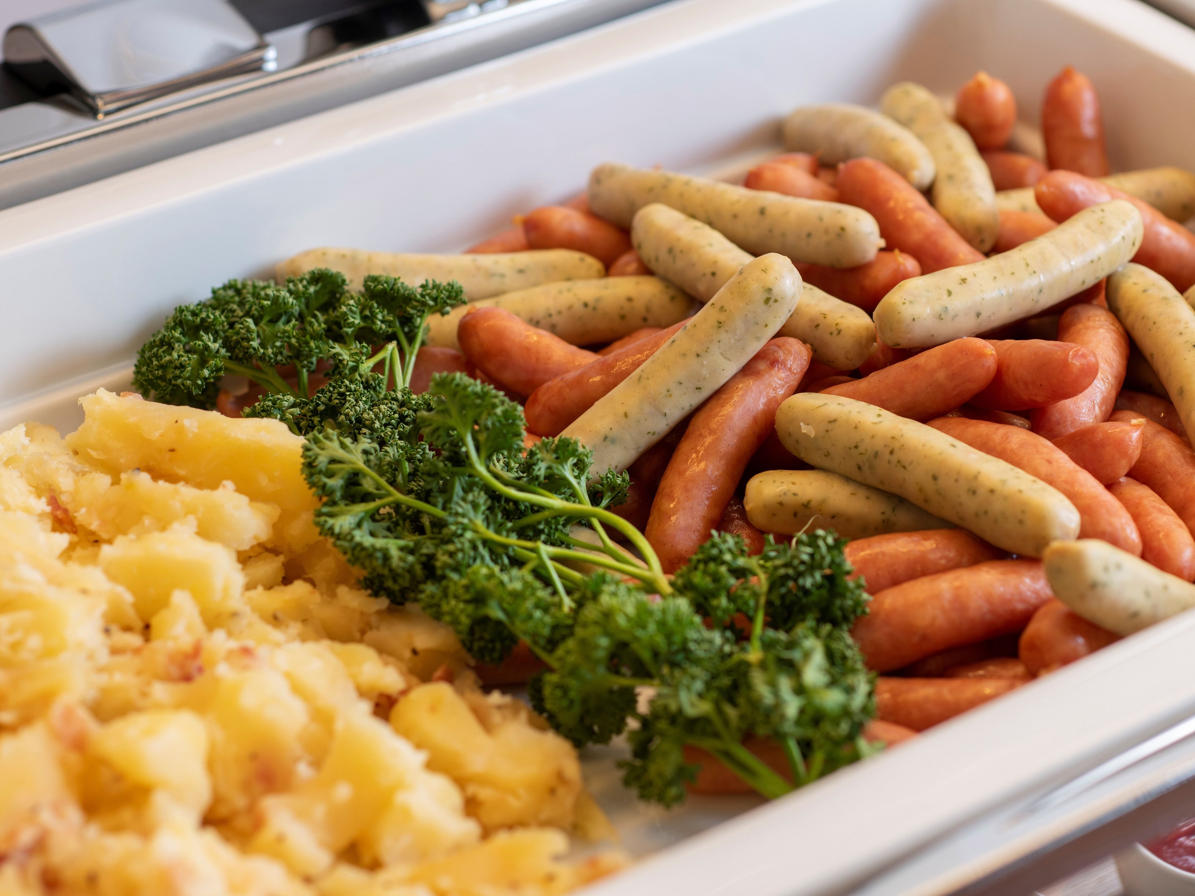 Een buffet met worstjes, wortels en aardappelpuree.