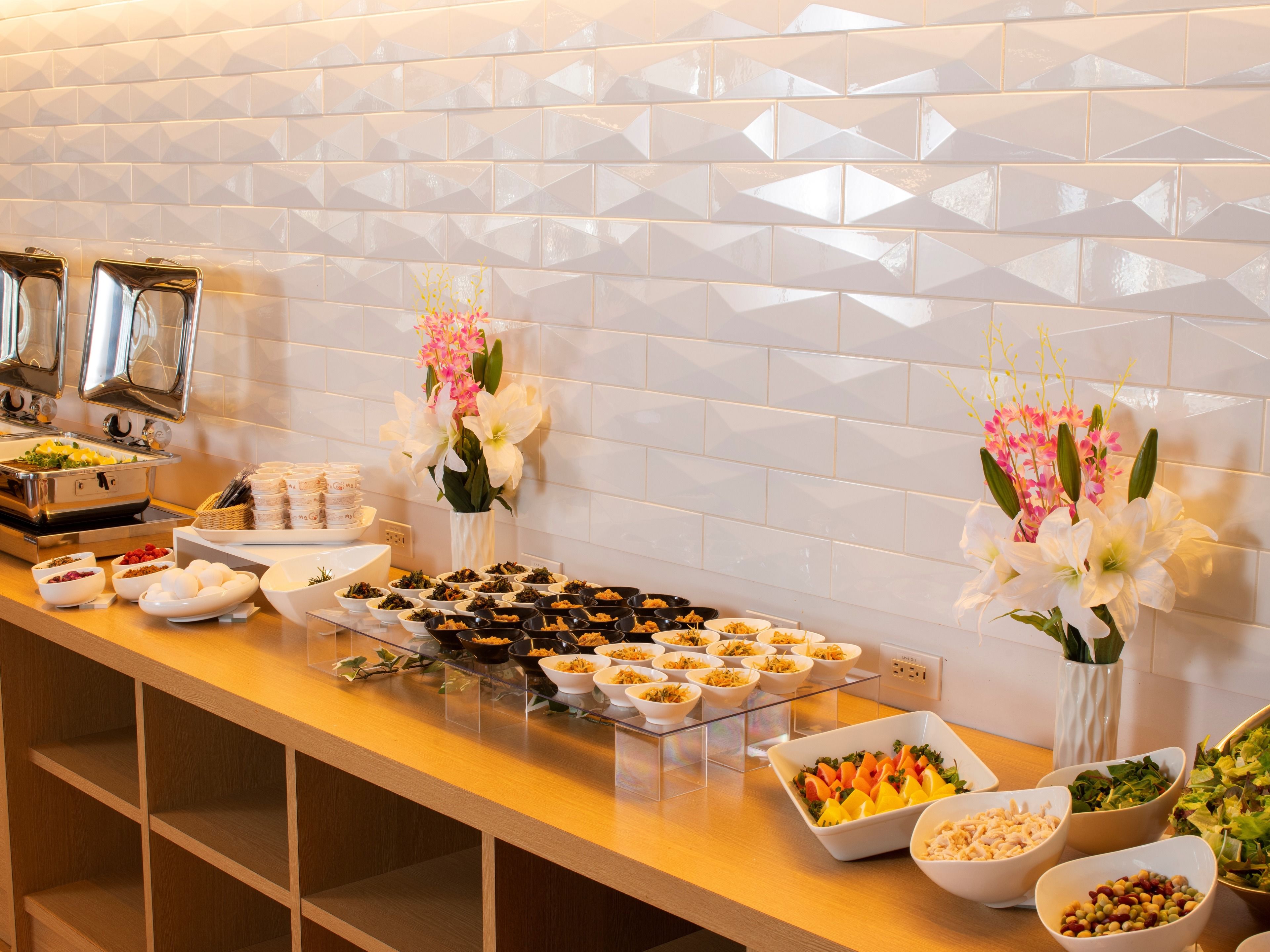 Un buffet proposant une variété de plats, notamment des fruits, des salades et des desserts, disposés sur un comptoir dont le mur arrière est recouvert de carreaux.
