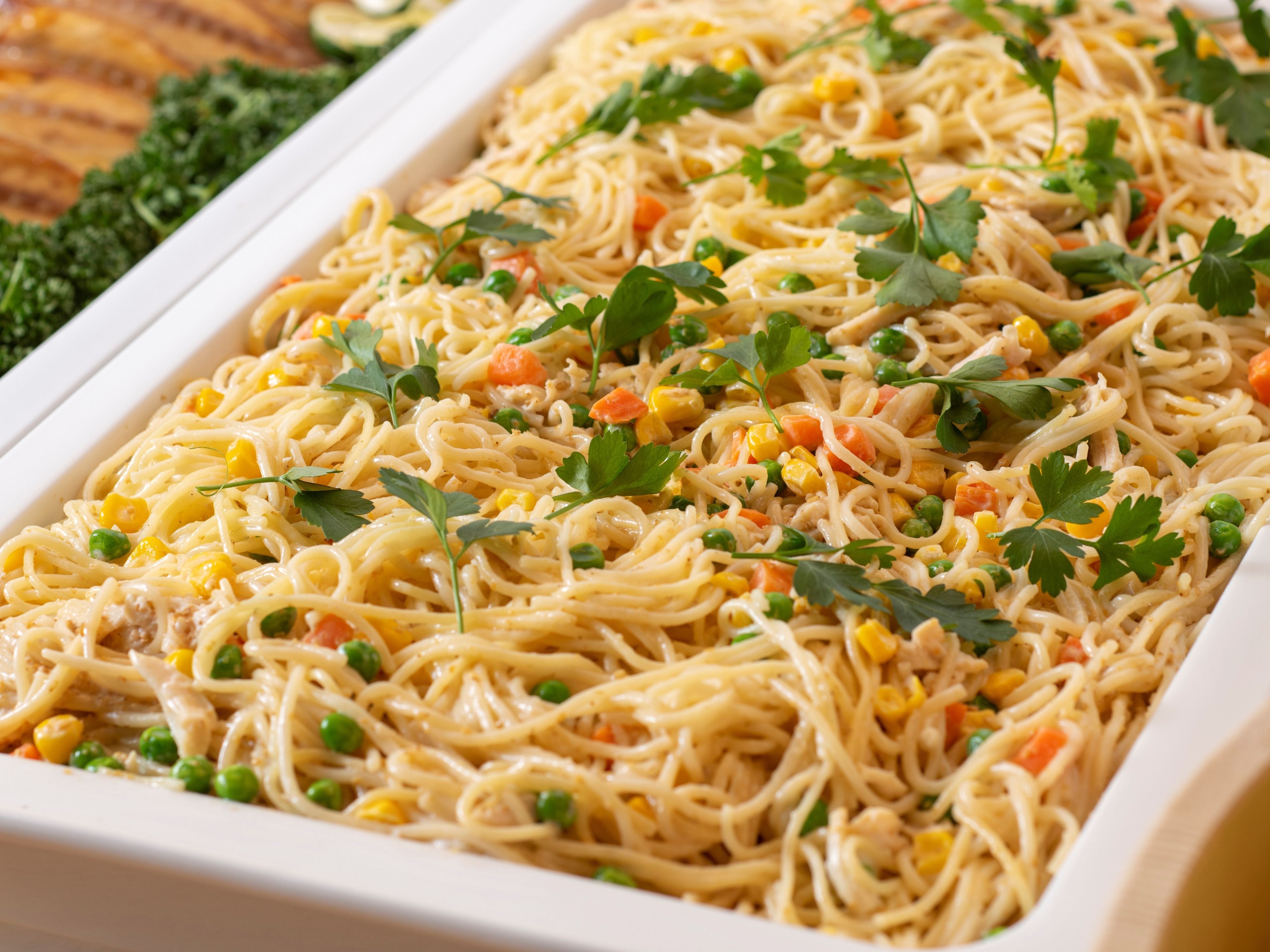 Eine rechteckige Servierschale mit Spaghetti, Erbsen, Mais und Karotten, garniert mit Petersilie.