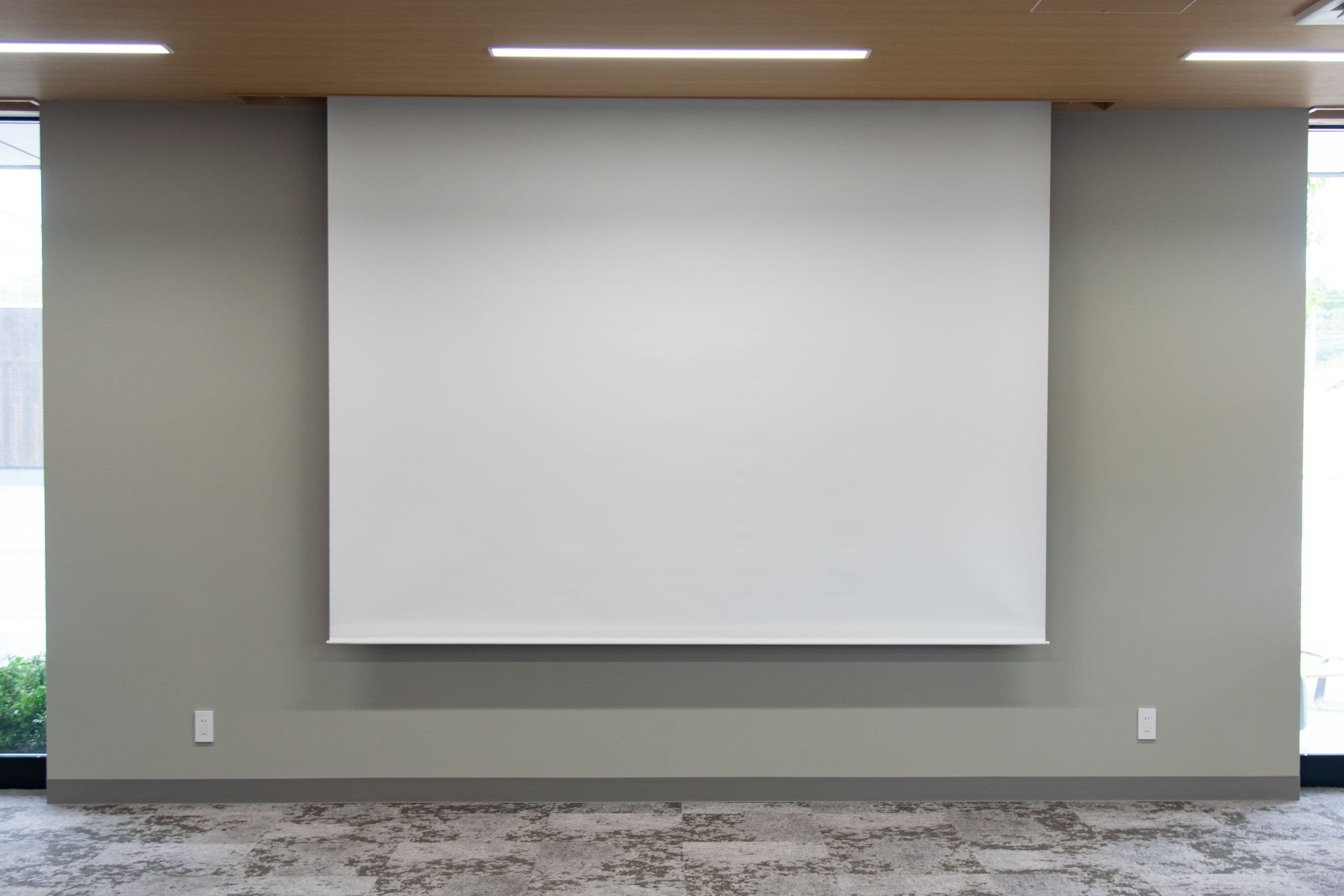 A room with a large whiteboard on the wall, a carpeted floor, and a window with a view of greenery outside.