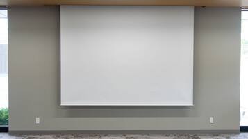A room with a large whiteboard on the wall, a carpeted floor, and a window with a view of greenery outside.