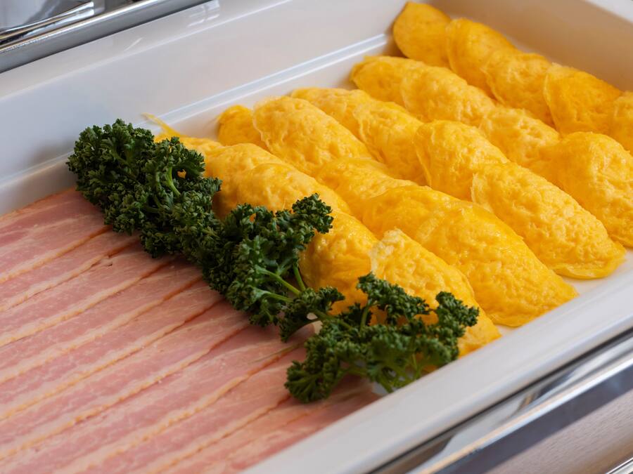 Una bandeja con huevos revueltos y tiras de tocino, adornada con perejil.