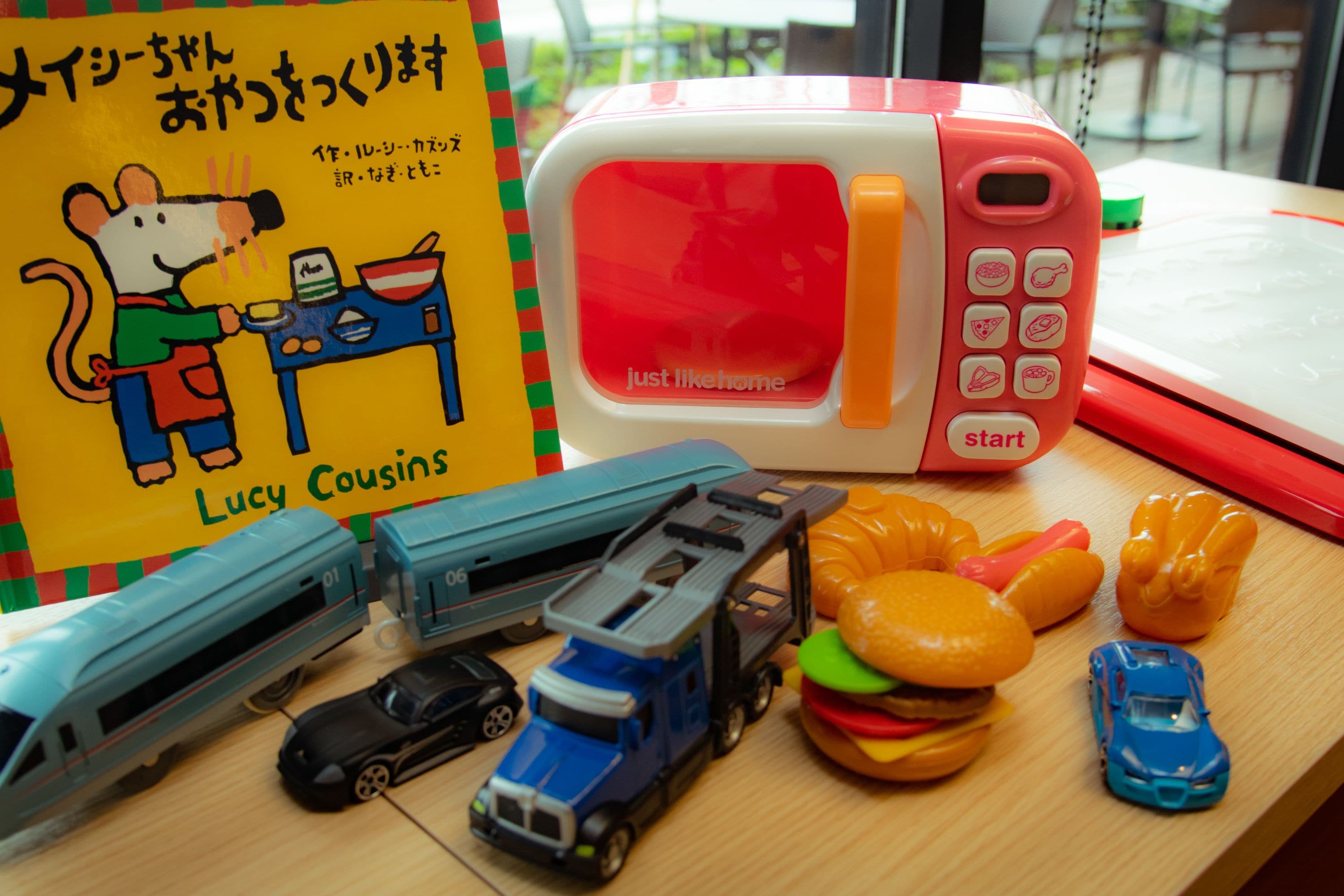 A table with a children's book, a microwave, toy vehicles, and a toy burger.